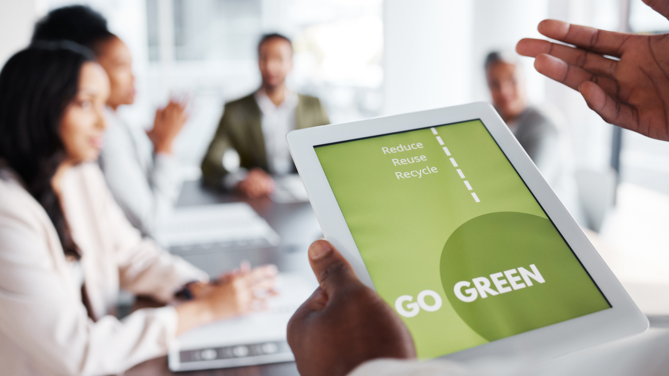 image of people sitting around a meeting table listening to a presentation about greener practices